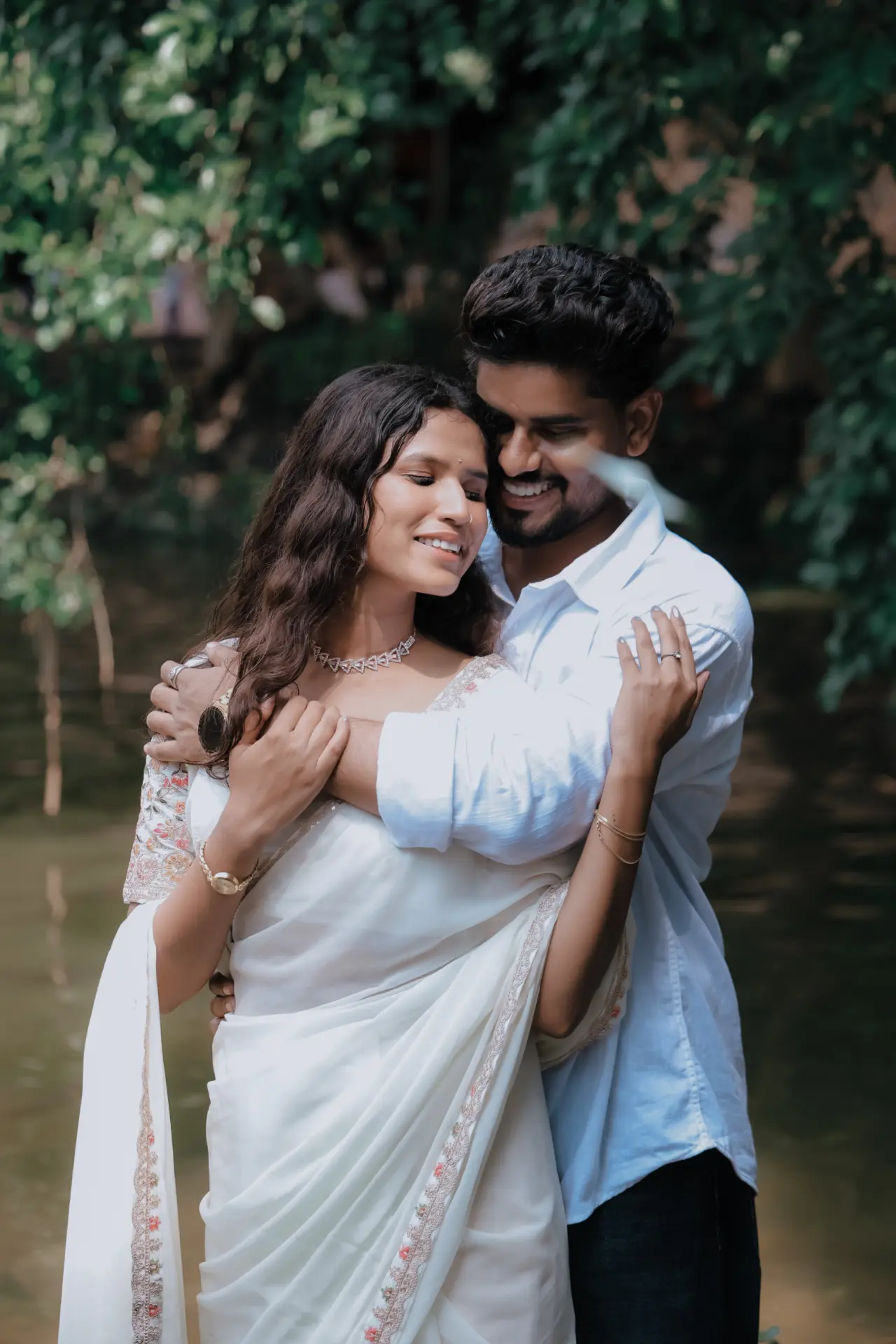 Pre-wedding couple embracing in white outfits by a riverside