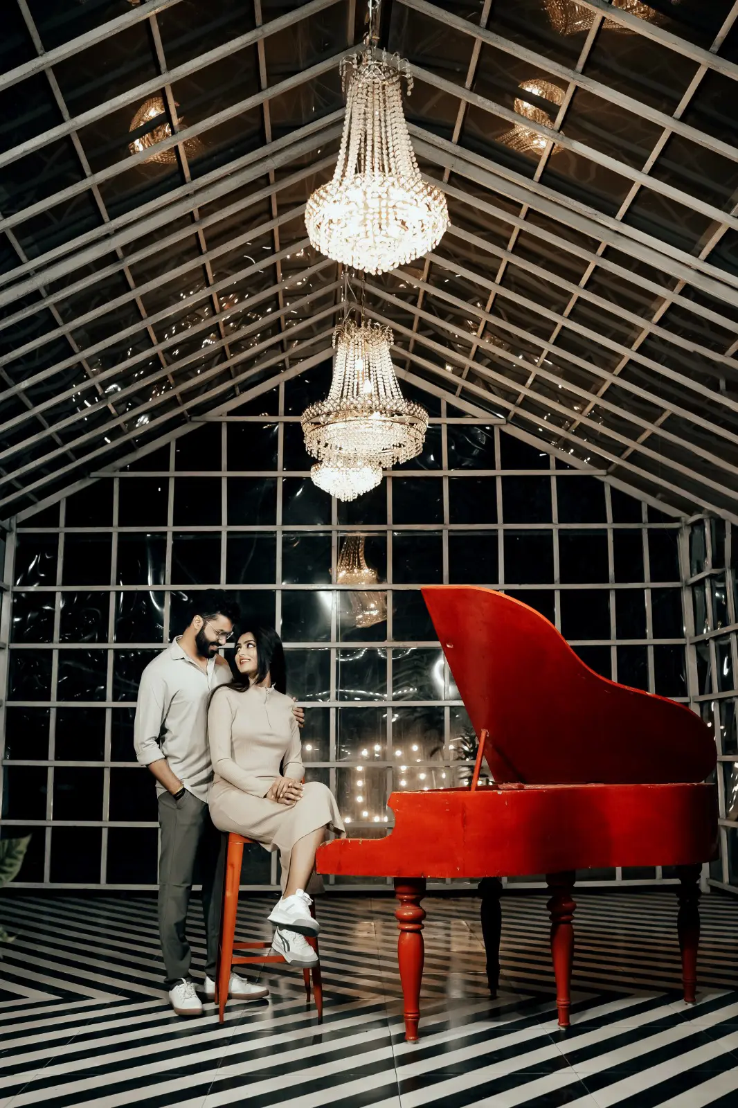 Pre-wedding couple by a red grand piano under chandeliers