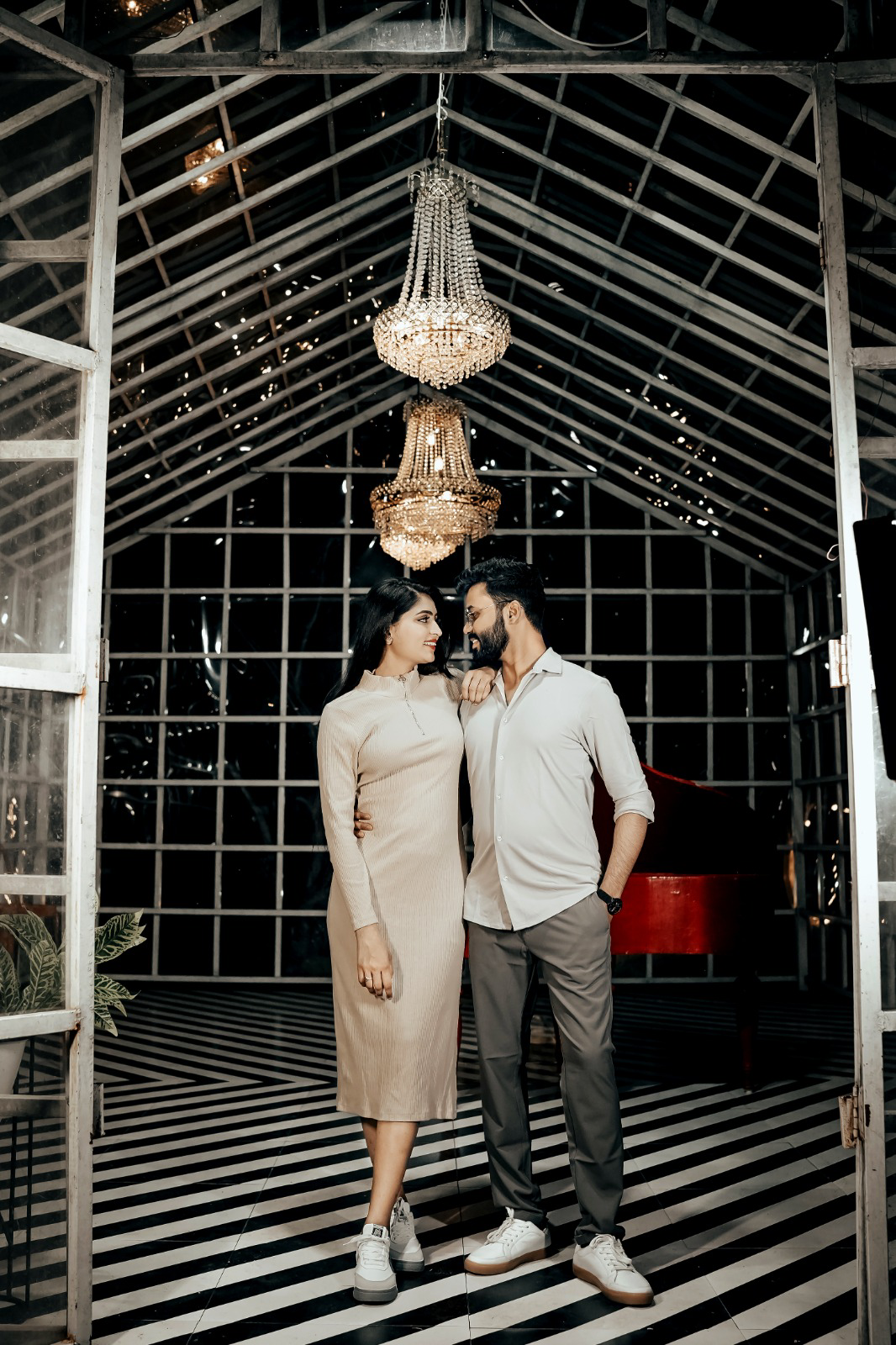 Pre-wedding couple beneath chandeliers in an elegant glasshouse