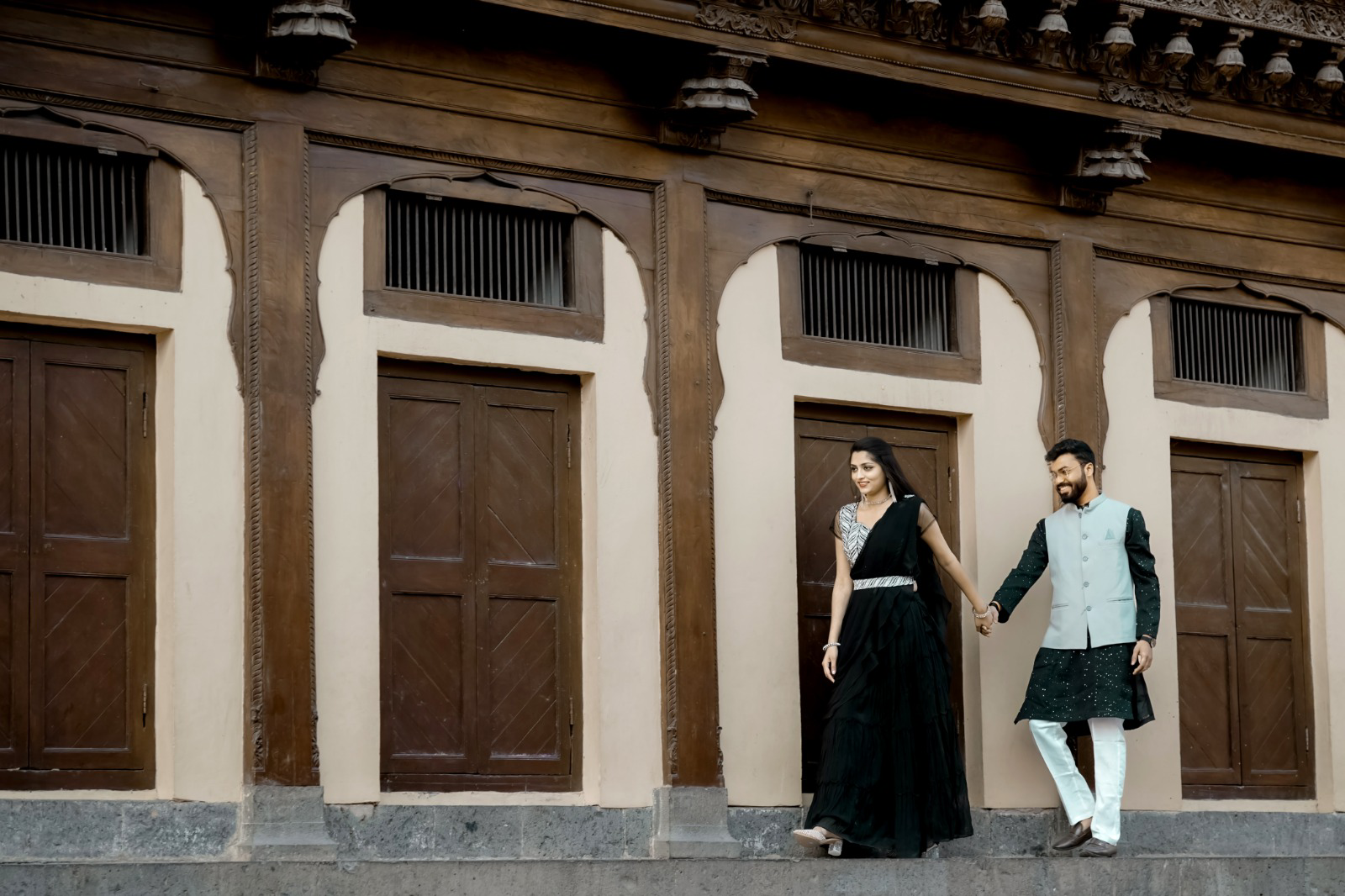 Pre-wedding couple walking hand in hand past carved wooden doors