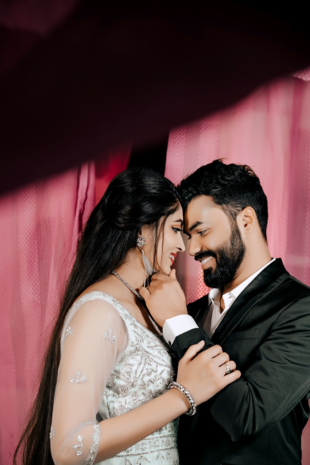 Pre-wedding couple in evening attire under soft pink drapes