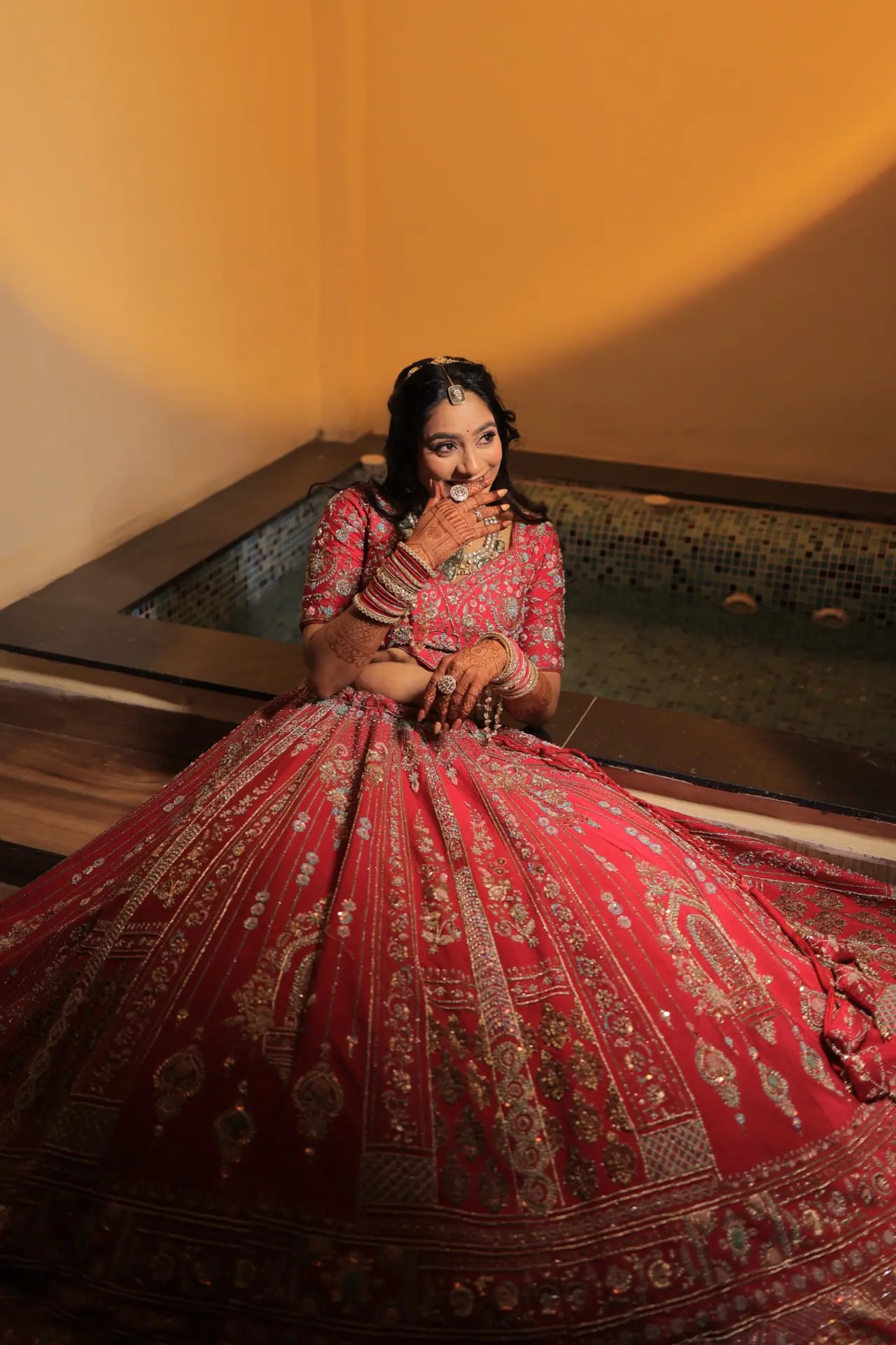 Bride in a red embroidered lehenga against a warm golden wall